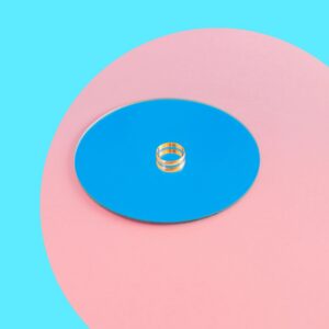 One golden wedding ring on round mirror in pink and blue colors.